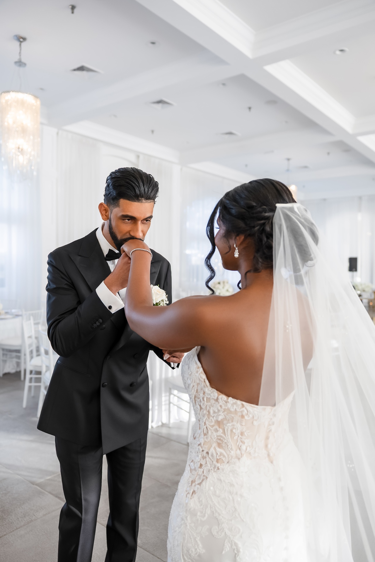 Boston wedding portrait — groom kissing bride's hand in an all-white ballroom